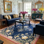 Living room with floral wallpaper, blue sofa, and decorative blue tufted wool rug.